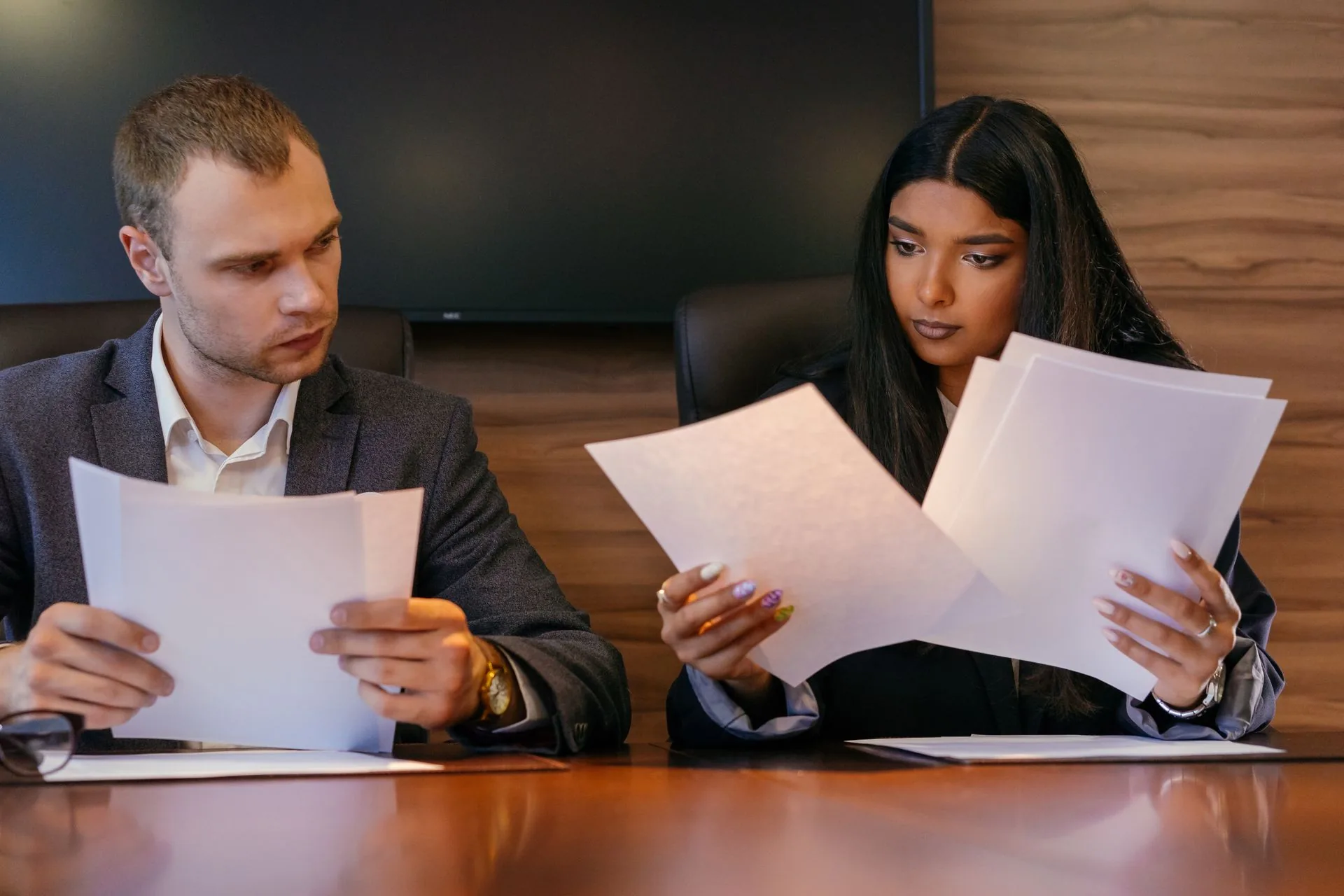 Duas pessoas analisam documentos em uma mesa de reunião.