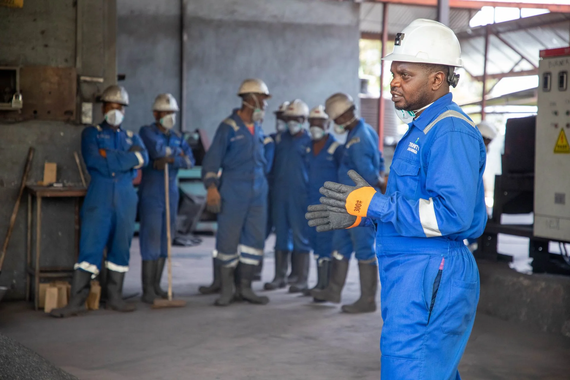 Grupo com capacetes e uniformes acompanha uma orientação em ambiente industrial.