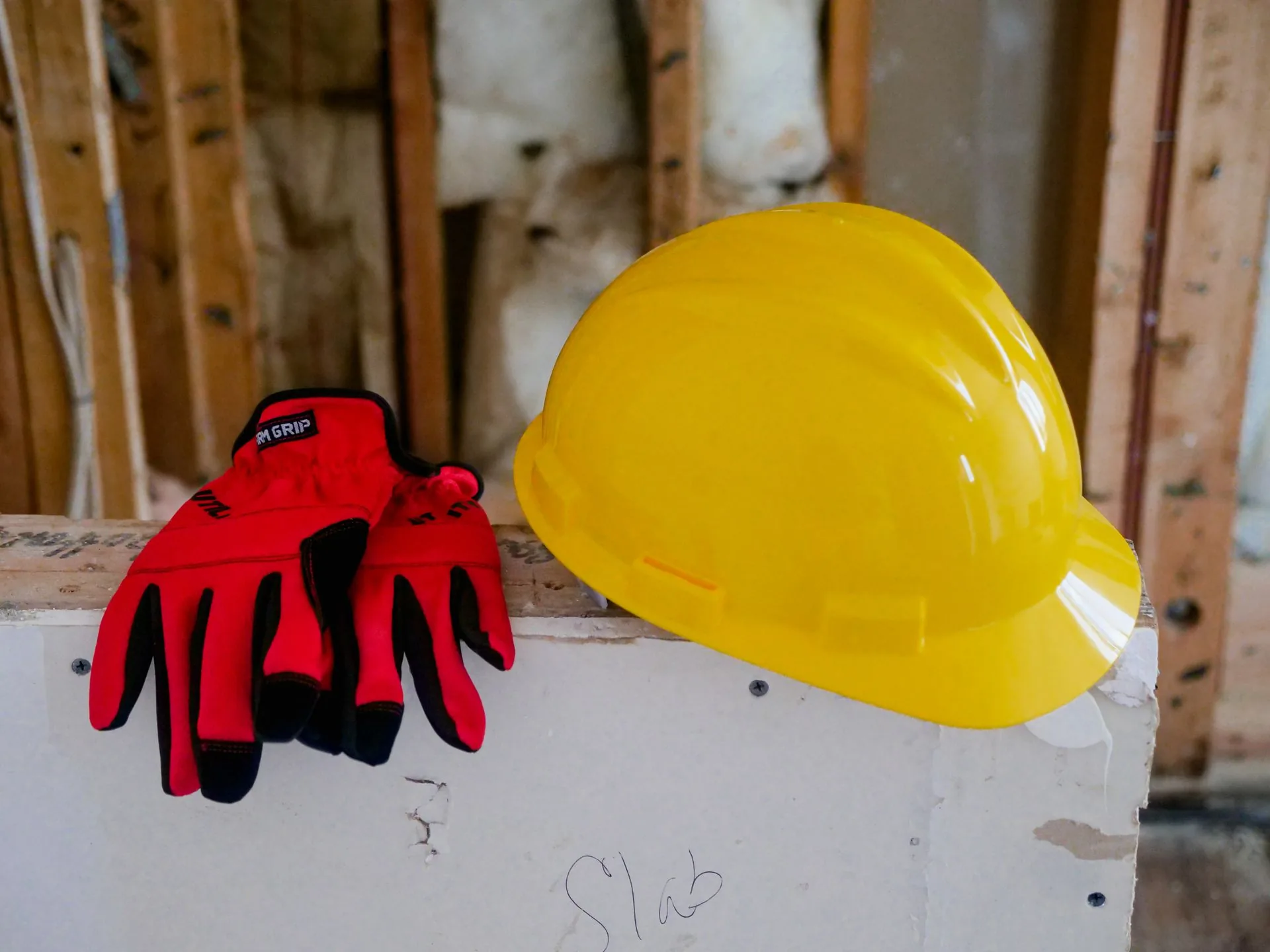 Capacete amarelo e luvas de proteção vermelhas em uma obra.